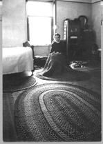SA0027 - Sarah Collins was from the South Family. She is shown braiding a rug. A bed and rug are visible in the photo. Identified on reverse., Winterthur Shaker Photograph and Post Card Collection 1851 to 1921c